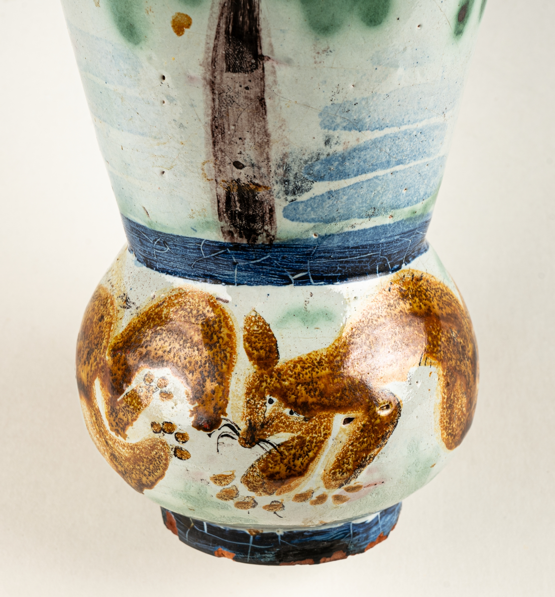 Vas, övre delen glaserad med trädmotiv i grönt, blått och brunt. Den nedre delens motiv föreställer springande ekorrar. Formgiven av Märta Willborg, 1930.