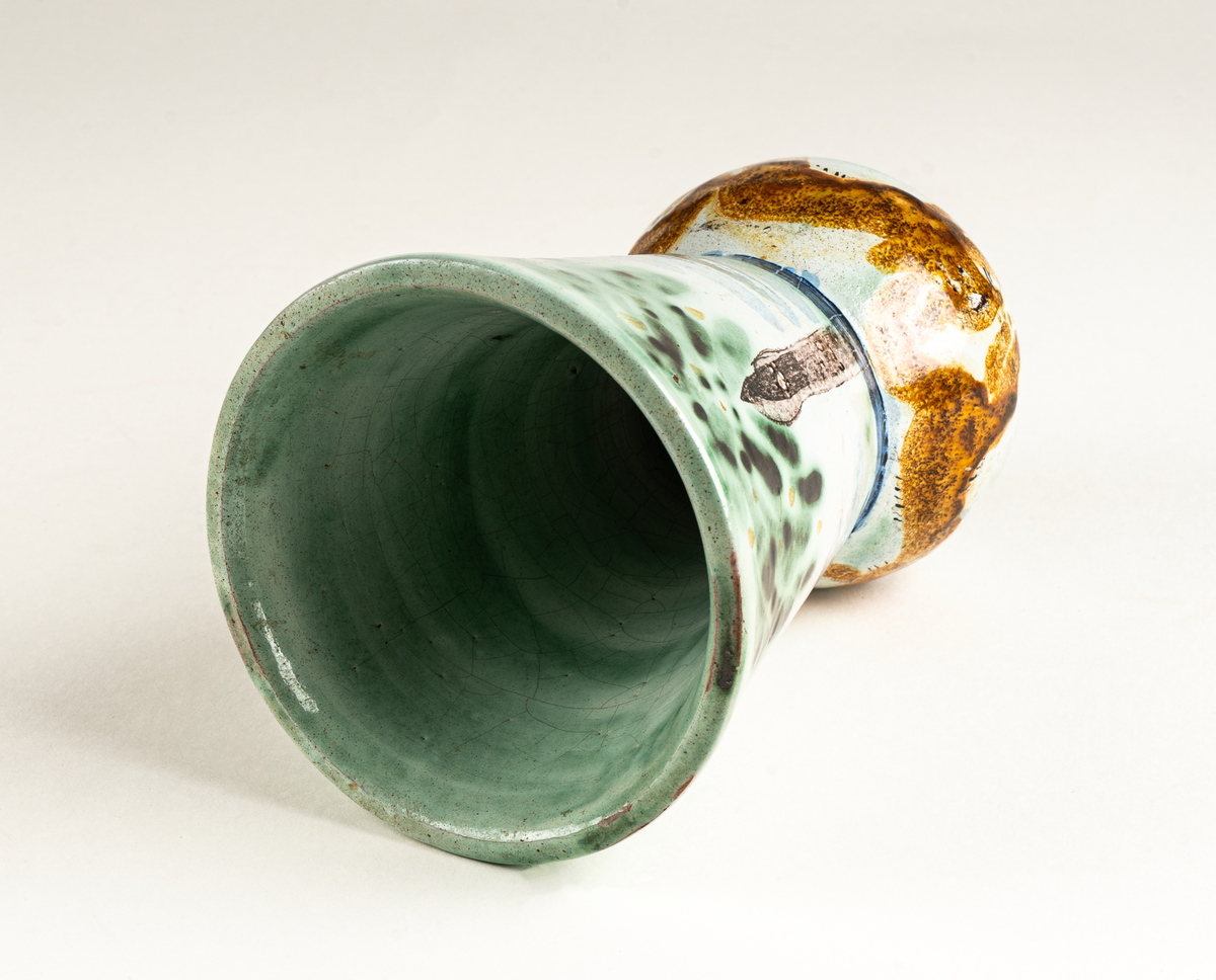 Vas, övre delen glaserad med trädmotiv i grönt, blått och brunt. Den nedre delens motiv föreställer springande ekorrar. Formgiven av Märta Willborg, 1930.