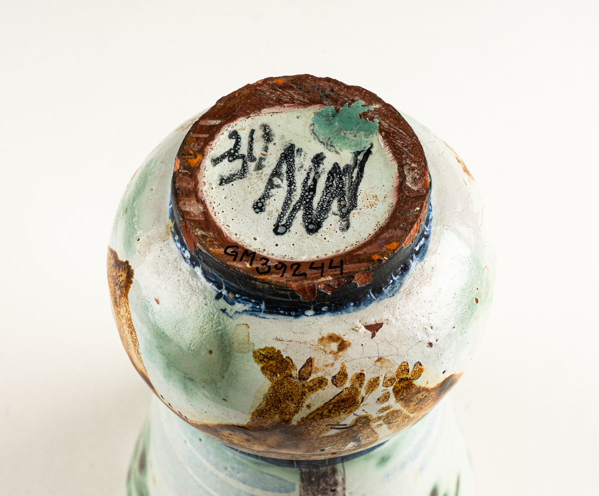 Vas, övre delen glaserad med trädmotiv i grönt, blått och brunt. Den nedre delens motiv föreställer springande ekorrar. Formgiven av Märta Willborg, 1930.