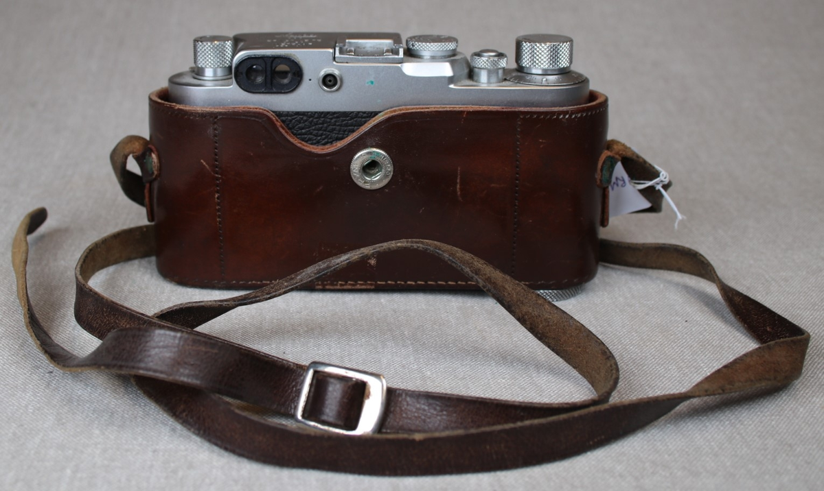 Fotografiapparat i skinntaske med bærehempe. Bruksanvisning medfølger.