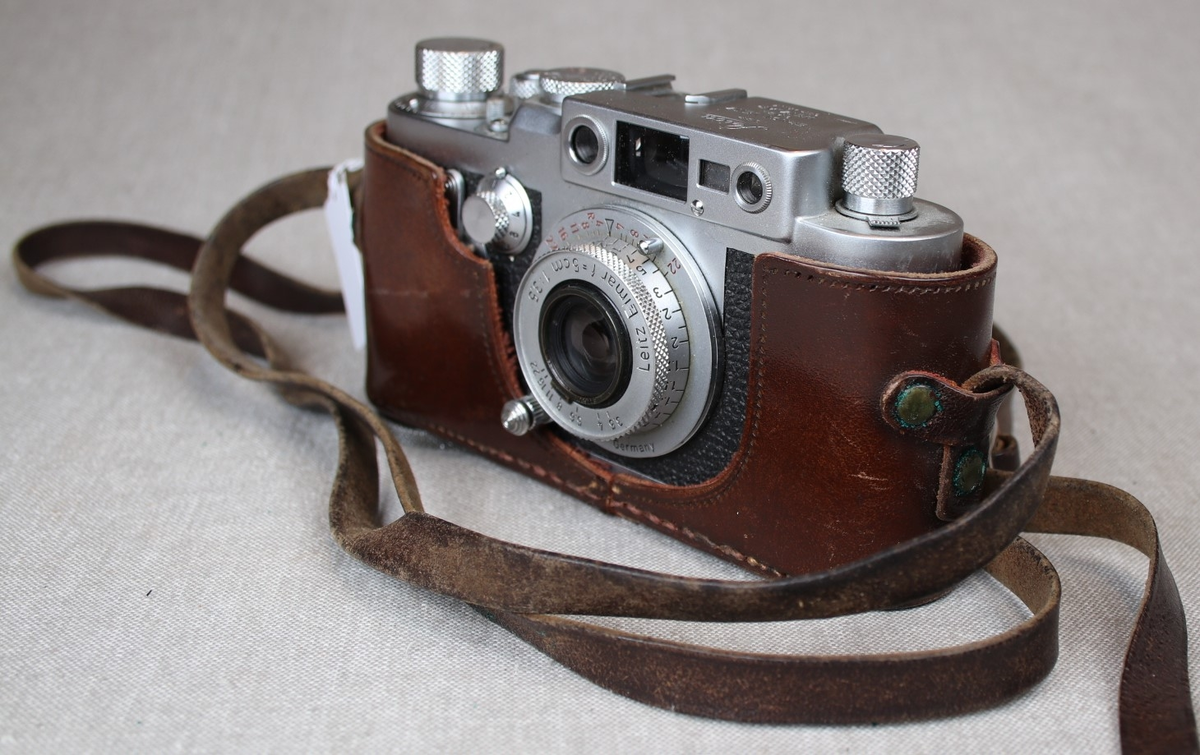 Fotografiapparat i skinntaske med bærehempe. Bruksanvisning medfølger.