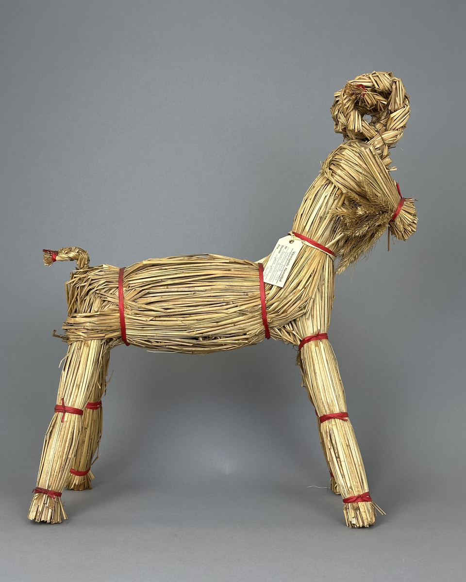 Julbock av halm, flätad och knuten med röda papperssnören.