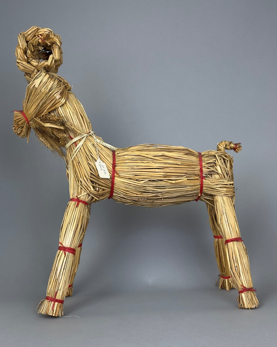 Julbock av halm, flätad och knuten med röda papperssnören.