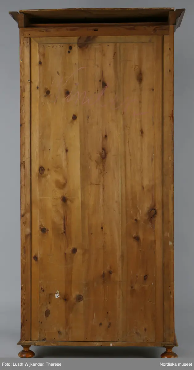 Inventering Sesam 1996-1999:
L 79 cm, B 46 cm, H 174 cm
Dockskåp av brunbetsat furu. Skåp med ett par glasdörrar med brun dekorrand på ramarna, undertill en låda med två dragknoppar, rakt krön med profilerad list. Skåpet står på fyra kulfötter. Dörrparet med lås och nyckel. På gavlarna 4 st fönster på vardera sidan. I skåpet 4 st våningar med sammanlagt 7 rum. Samtliga rum med mönstrade papperstapeter och krok i taket för lampa.
VÅNING 1: 1 rum, heltäckningsmatta av blåmönstrat tyg på vit botten. På höger kortvägg 3 st små pappersbilder i färgtryckav liten flicka i olika situationer. På  bakväggen en europakarta med tysk text.
VÅNING 2:  2 st rum. Bägge med mönstrade linoleummattor och två fönster. Gråmålad dörr mellan rummen. Vänster rum; Spiskåpa av vit papp på bakväggen. 2 st gardinlufter av vit spets med kornischer av gulmetall med påklistrad guldpappersremsa med mönster i relief. Höger rum; två gardinlufter av brunrandigt tyg, kornischer som ovan, omtag av metallkedjor på ena luften och rosa sidenband på andra. Ovanför dörren sitter 3 st beslag av pressad plåt. En större med måne och blommor och två mindre med sköld och blommor. 
VÅNING 3: bägge rummen med mönstrad heltäckningsmatta med lugg och två fönster. Vänster rum; 2 gardinlufter, 1 sänghimmel och 1 draperi av blått siden med vit kantspets. Gardiner med kornischer som ovan. 5 st omtag i form av snodd av gulmetall. Höger rum; enfärgade röda tapeter,2 st gardinlufter av rödrandigt siden med omtag av samma tyg, undergardin av vit spets, kornischer som ovan. Ett draperi av rött och randigt (i flera färger) ylle med ett omtag av metallkedja.
VÅNING 4: Vänster rum; flerfärgat och småmönstrad linoleummatta, Höger rum; utan golvbeläggning. 
- Ett par gröna gardiner av stärkt bomull, som ursprunglingen har suttit innanför glasdörrarna på dockskåpet. Rynkade i båda kortändorna. B 46,5, L 128 cm
Har tillhört givaren. (född 1886 enl. adelskalendern). 
Inventarier till dockskåpet inv.nr 164571-164728
Leif Wallin nov 1997