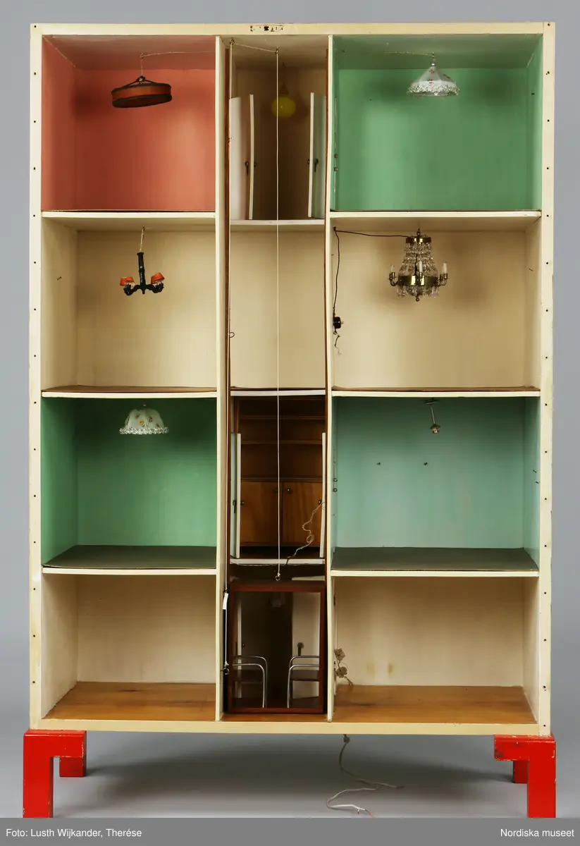 Inventering Sesam 1996-1999:
B 77,5, Djup 36,0, H 119,0 cm
Dockskåp av furu med mellanväggar av plywood, målat i gräddgult, fasaden "putsad" med färg blandad med sågspån. Dockskåpet har dubbeldörrar med lås och en fasad på gångjärn med en dörr och 10 fönster, inspirerad av det första kollektivhuset i funkisstil på John Erikssons gata. Dockskåpet är befolkat av fam. Björnerholm. Gunvor Svartz-Malmberg f. 1925-6 var ca 10 år när hon fick skåpet. 
LS 85
Helena Carlsson