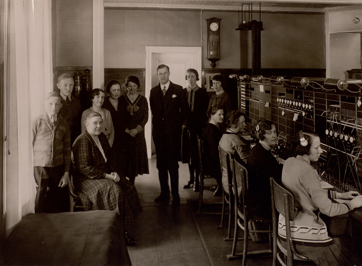 Piteå telefonstation år 1932. Telefonsal. Gruppfoto. Telegrambud Sven Holmberg. K.E. Hertlander, rikstelefonist H. Sundqvist (sittande), telegrafexpeditör  A. Holmgren, landstelefonist R. Ekberg, lokaltelefonist G. Bergman, Telegrafkommissarie S.A. Hydén, lokaltelefonist E. Forsman, rikstelefonist J. Engström, rikstelefonist I. Bucht, rikstelefonist A. Pettersson, lokaltelefonist J. Berglund, lokaltelefonist E. Ekberg.