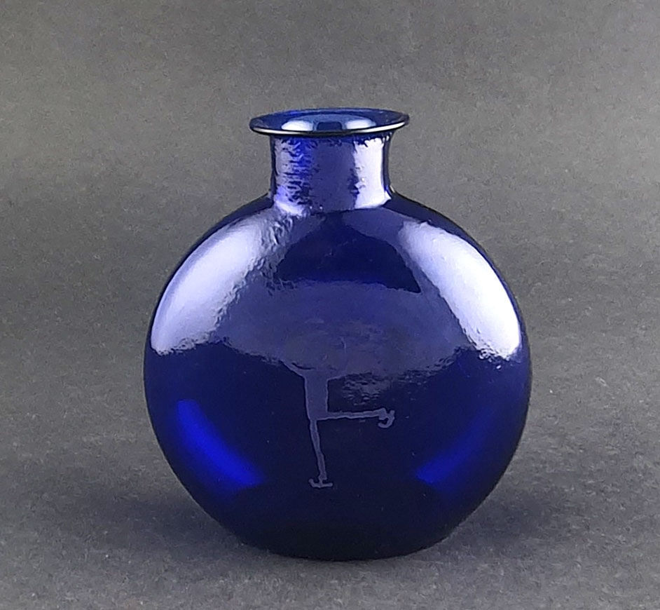 Blå glassflaske med rund korpus. På den ene siden emblemet for Lillehammer '94, og på den andre siden piktogrammet for kunstløp.