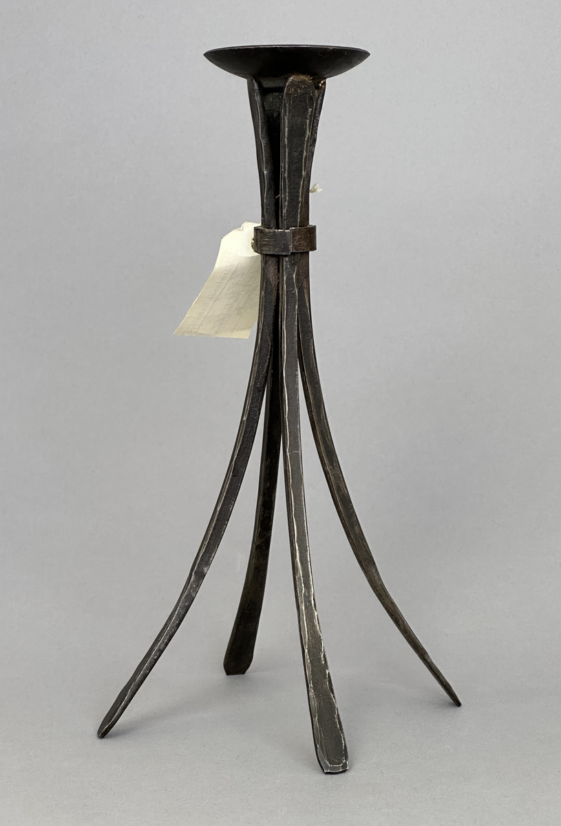 Ljusstake "Lars" av järn för ett ljus. Fyra fyrkantsstänger har sammanfogats i ena änden med en ljusmanschett och en bit nedanför hålls de ihop av en ring.