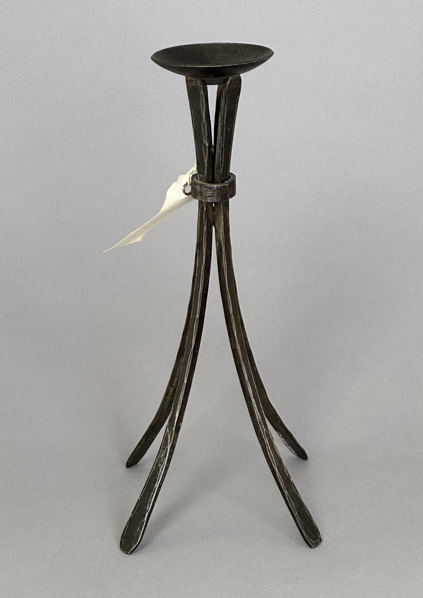 Ljusstake "Lars" av järn för ett ljus. Fyra fyrkantsstänger har sammanfogats i ena änden med en ljusmanschett och en bit nedanför hålls de ihop av en ring.