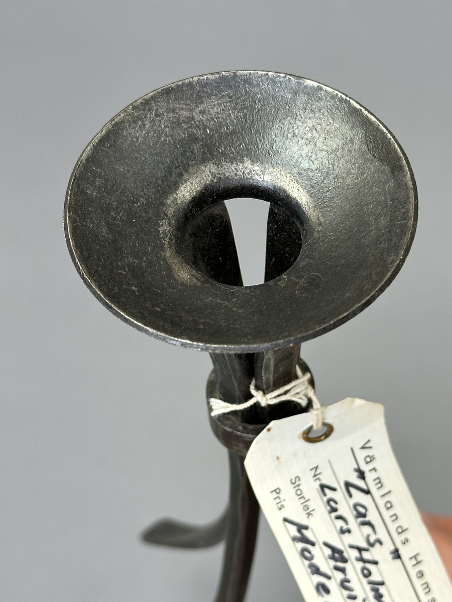 Ljusstake "Lars" av järn för ett ljus. Fyra fyrkantsstänger har sammanfogats i ena änden med en ljusmanschett och en bit nedanför hålls de ihop av en ring.