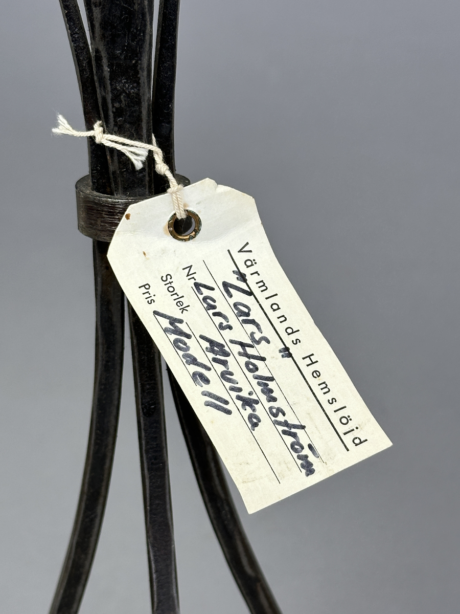 Ljusstake "Lars" av järn för ett ljus. Fyra fyrkantsstänger har sammanfogats i ena änden med en ljusmanschett och en bit nedanför hålls de ihop av en ring.