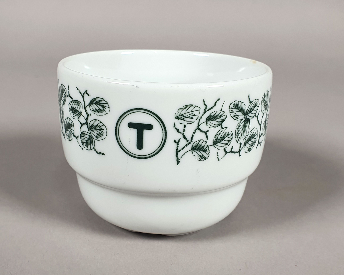 Hvit kaffekopp av porselen, med grønt bladmønster langs kanten og turistforeningens logo fra perioden etter 1988.