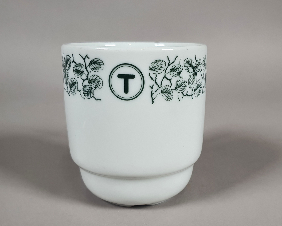 Hvit kaffe- eller tekopp av porselen, med grønt bladmønster langs kanten og turistforeningens logo fra perioden etter 1988.