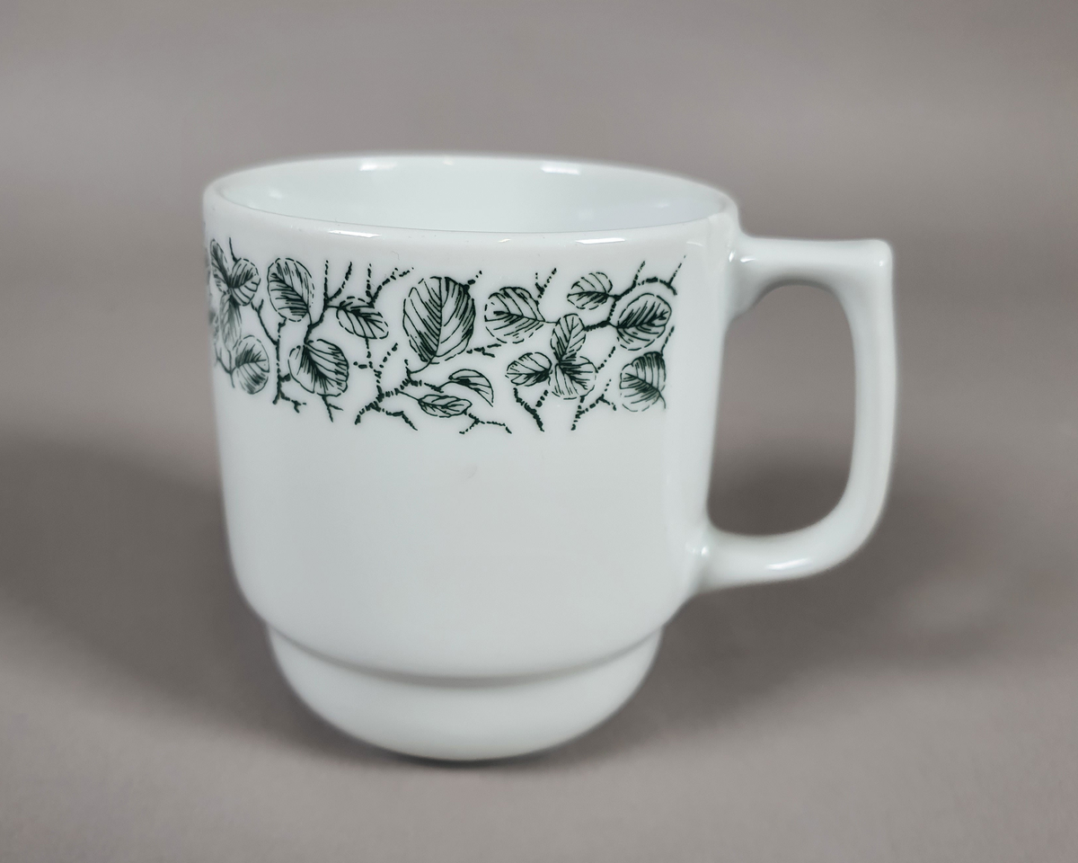 Hvit kaffe- eller tekopp av porselen, med grønt bladmønster langs kanten og turistforeningens logo fra perioden etter 1988.