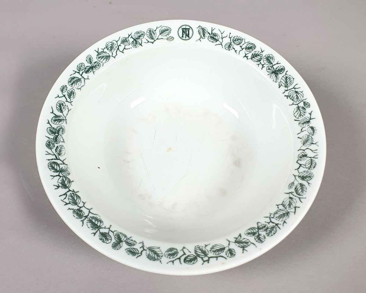 Hvit dyp tallerken av porselen, med grønt bladmønster langs kanten.