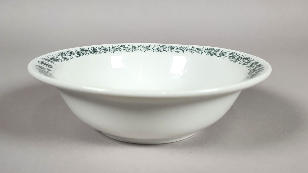 Hvit dyp tallerken av porselen, med grønt bladmønster langs kanten.