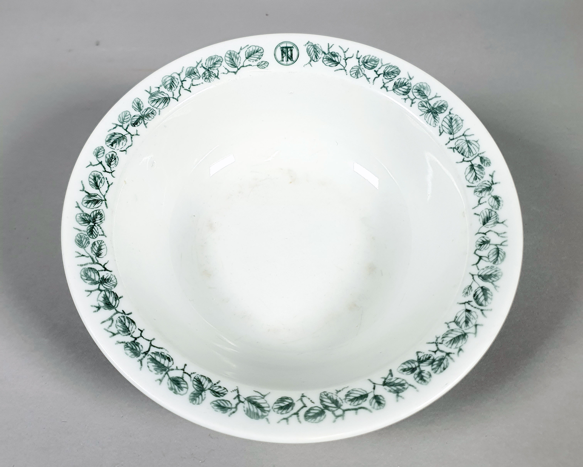 Hvit dyp tallerken av porselen, med grønt bladmønster langs kanten.
