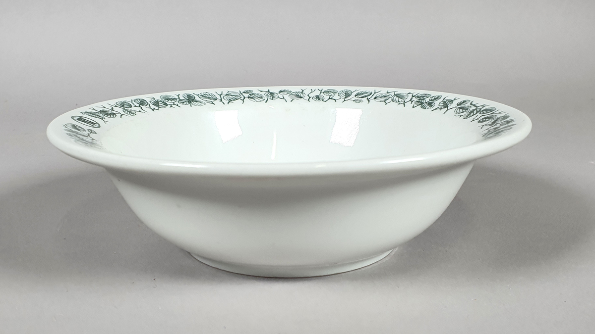 Hvit dyp tallerken av porselen, med grønt bladmønster langs kanten.

