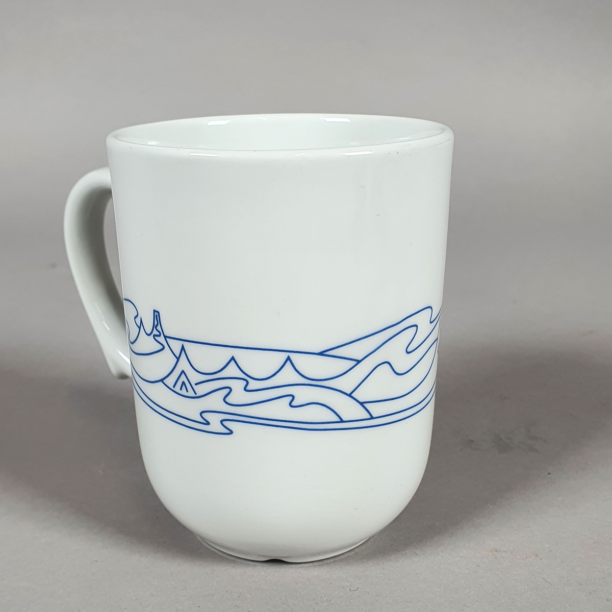 Hvit kopp av porselen, med med blått dekor (fjellmotiv) rundt korpus, og turistforeningens logo fra 1988