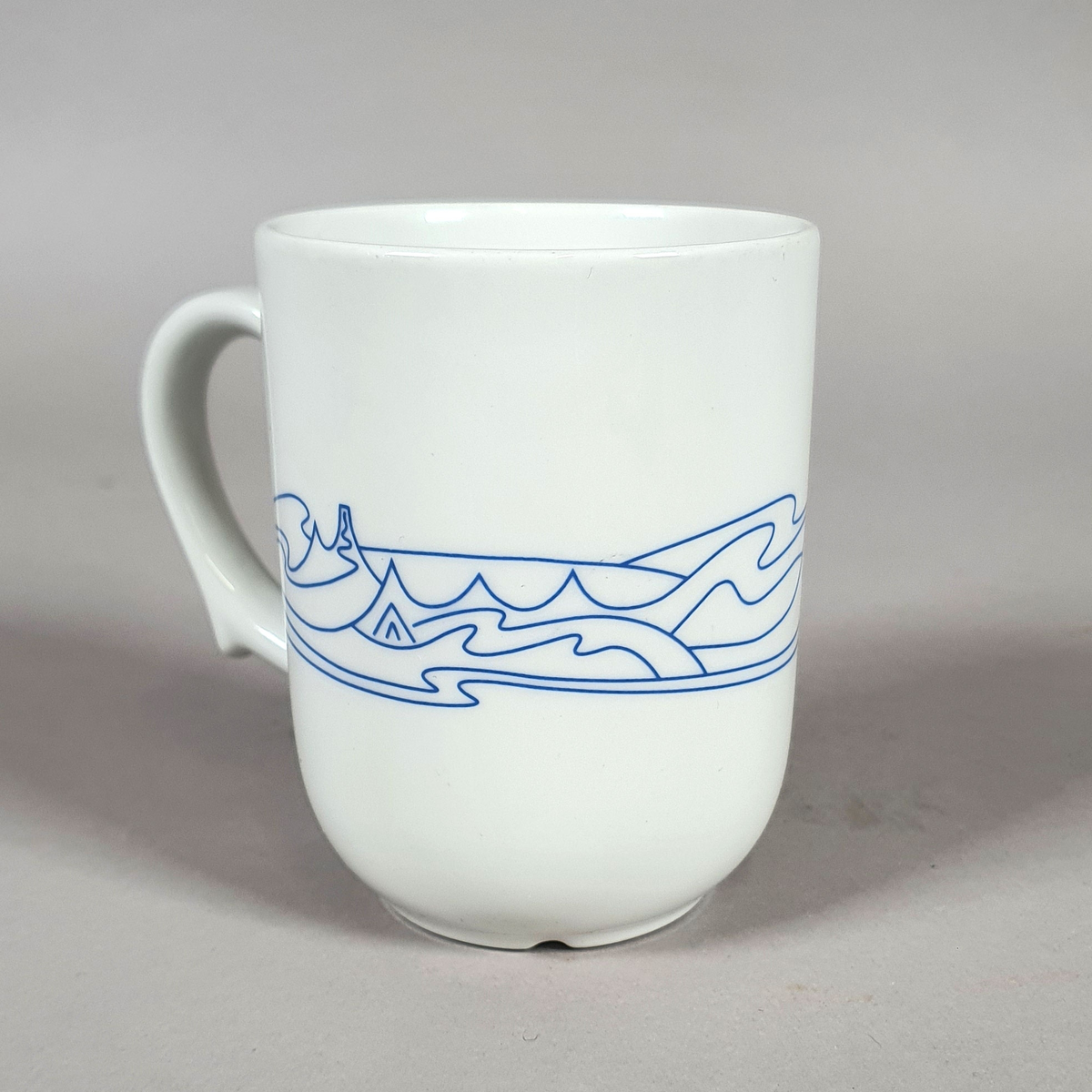 Hvit kopp av porselen, med med blått dekor (fjellmotiv) rundt korpus, og turistforeningens logo fra 1988
