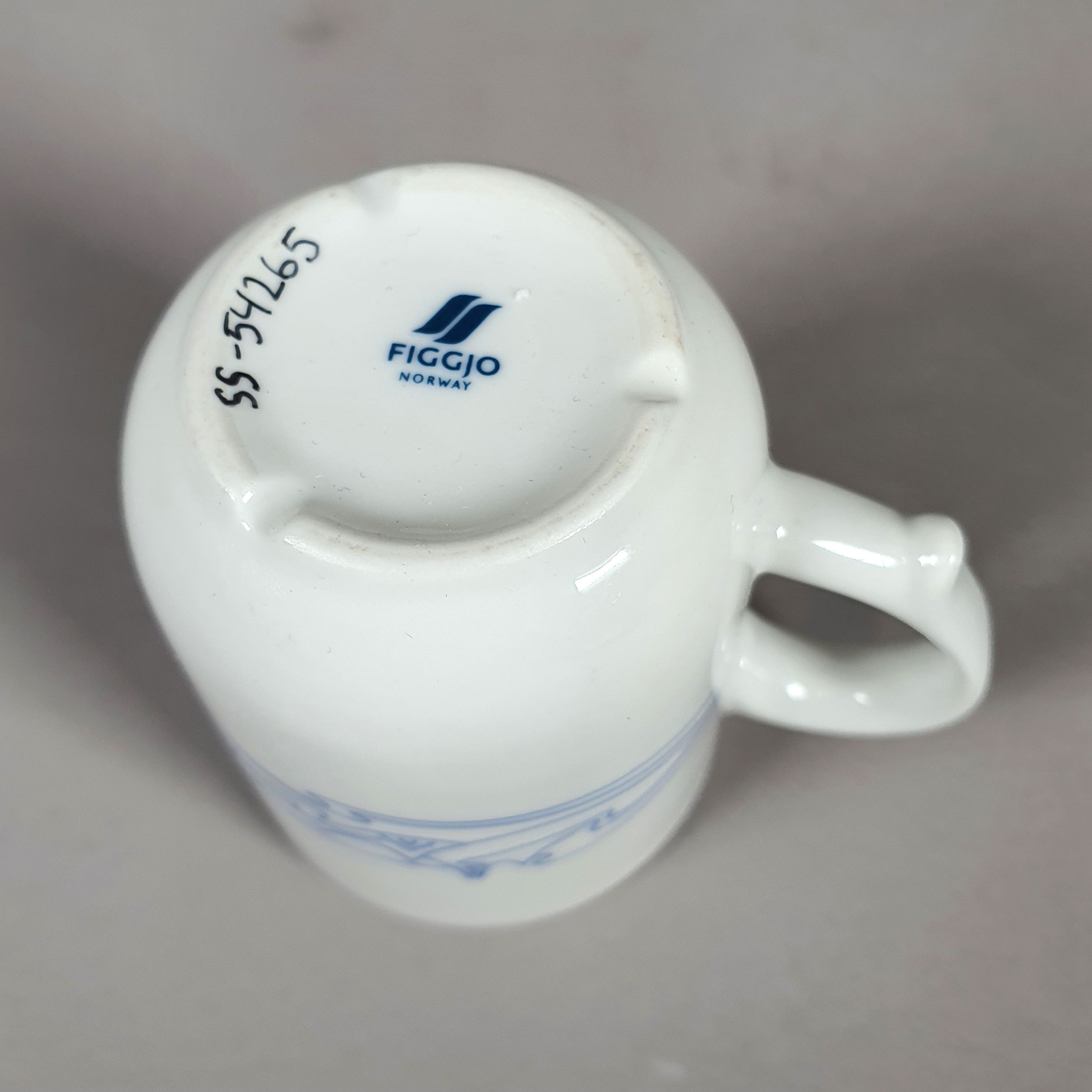 Hvit kopp av porselen, med med blått dekor (fjellmotiv) rundt korpus, og turistforeningens logo fra 1988
