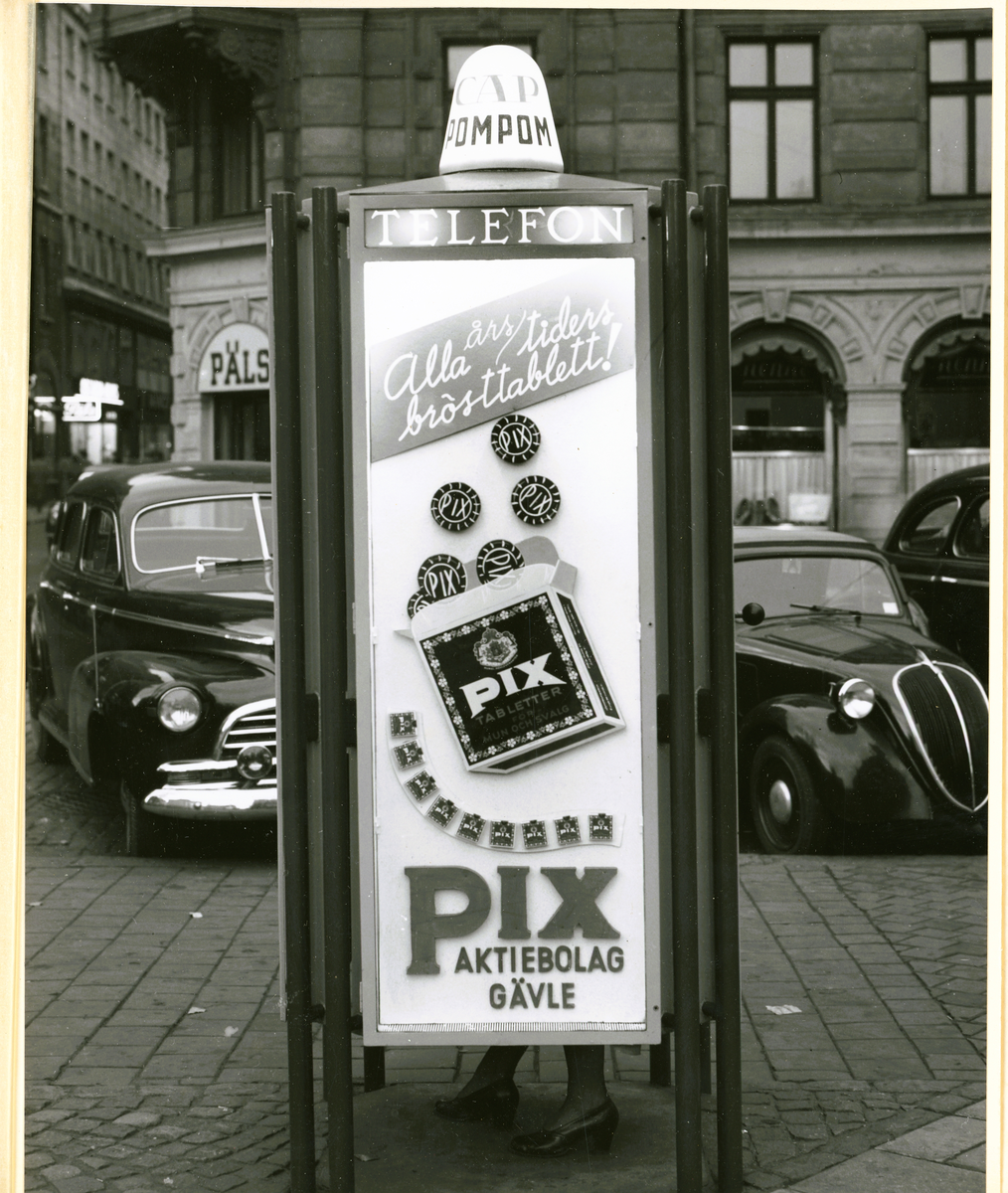 Ett fotokort som innehåller en svartvit bild av en reklamskylt för Pix tabletter, som är placerad på ett telefonbås. På baksidan av kortet finns en stämpel från Fotonova AB, och framsidan pryds av deras emblem. Kortet dateras till perioden 1949-50.