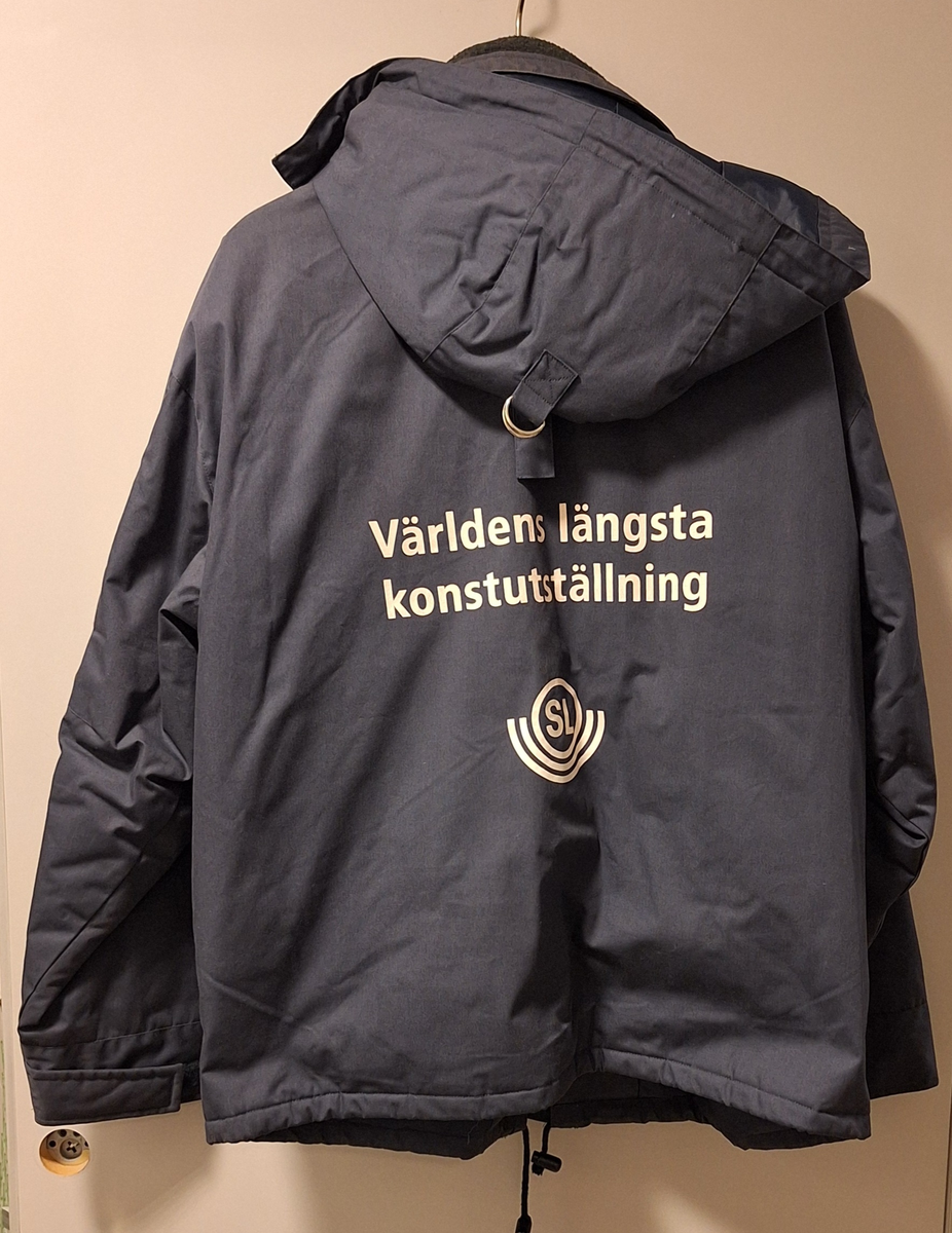 Marinblå jacka. Text på ryggen: SL Världens längsta konstutställning. Storlek M.