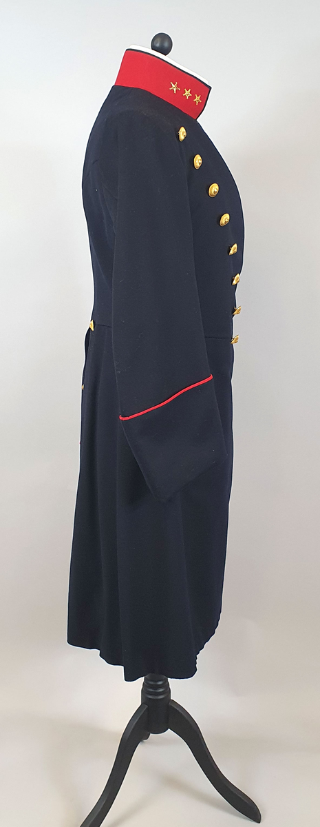 Mørkeblå uniformsfrakk av ull med rød krage med tre stjerner på hver side (kapteinsgrad). Løskrage av kartong på innsiden av kragen. Dobbeltspent med 8 gullknapper på hvert forstykke som er vattert. Frakken er innsvinget i livet og har splitt på ryggen med knapper og røde kantbånd. Rødt kantbånd på mansjettene. Svart fôr av bomull.