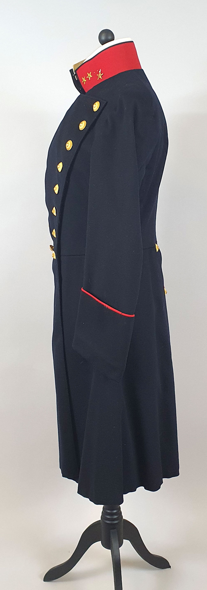 Mørkeblå uniformsfrakk av ull med rød krage med tre stjerner på hver side (kapteinsgrad). Løskrage av kartong på innsiden av kragen. Dobbeltspent med 8 gullknapper på hvert forstykke som er vattert. Frakken er innsvinget i livet og har splitt på ryggen med knapper og røde kantbånd. Rødt kantbånd på mansjettene. Svart fôr av bomull.