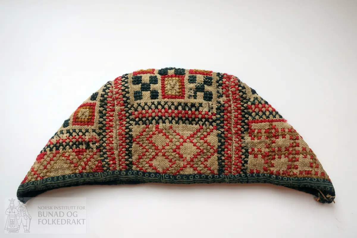 Barnehue. Trestykkshue med midtstykke og sidestykker. Midtstykket har ein skøyt på bakstykket, ca. 3 cm opp frå kanten. Hua er laga av lin med krosstingsbroderi i blått, raudt, lys grønt og gulbrunt over 3x3 trådar. Saumane inne i hua syner at dette er ombruk. Hua er kanta med blått bomullsstoff med lyseblått mønster, 0,6 cm breitt på retta og 0,9 cm på vranga, sydd på rette mot rette på retta, bretta over til vranga og sydd med kvit tråd, bomull? Fôr i grått bomullsstoff med små blomster i svart og kvitt.  Ytterstoff og fôr er sydd saman med ein saum 0,4 mm brei, bretta til kvar side og sydd ned. Ingen knyteband, men på eine sida ein liten rest av kvardingen, kanskje den er ein rest av eit knyteband?