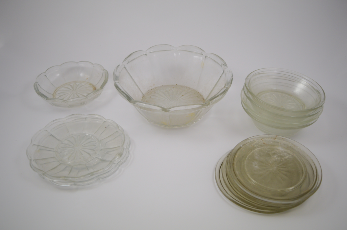 13 stk. runde glass fat av 5 ulike typer. To typer glassasjetter: 2 stk. med fasetter som minner om kronblader og bølgete kant, 4 stk. rette med forhøyet kant ytterst. Tre typer glasskåler: 1 stk. med fasetter som minner om kronblader og bølgete kant. 3 stk. med fasetter i bunnen, men rett kant, 1 stk. med kløverdekor i bunnen og rett kant. En type glassbolle med fasetter som minner om kronblader og bølgete kant.