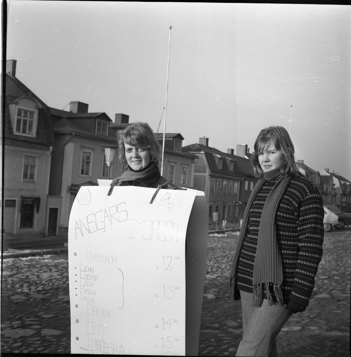 Två flickor på Gränna torg, den ena med s k sandwich-reklam för Ansgarkretsens sportlovsarrangemang.