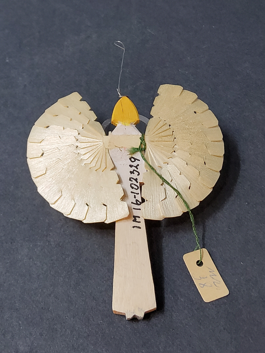 Spånängel, par med kropp av trä, vingar av spån. Två storlekar, den större med grön överde,l gult hår, resten trävitt, i botten liten platta. Den mindre vitmålad kropp, gult hår, vingar i trävitt, metalltråd för upphängning.