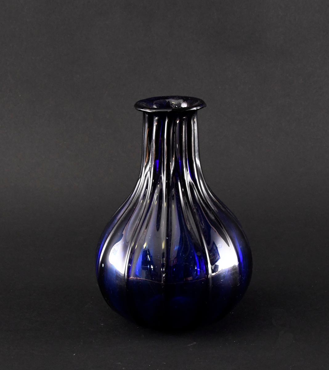 Karaffel av håndblåst glass. Karaffelen har kuleformet korpus med utstående kanneleringer. Blått glass.