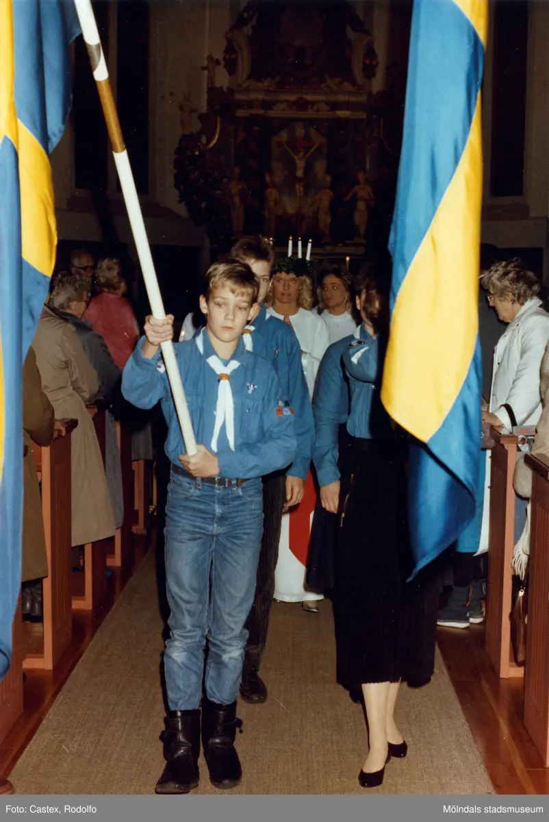 Kröningen av Mölndals Lucia i Fässbergs kyrka i december 1985. Lucian och tärnorna tågar ut ur kyrkan. Före går två scouter som fanbärare.