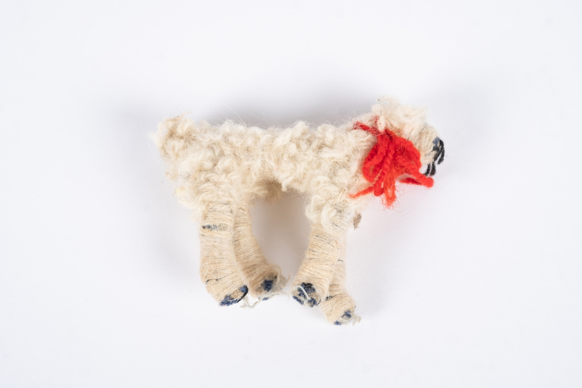 En hundefigur laget av tekstil og ull. Hunden er hvit med et rødt halsbånd.