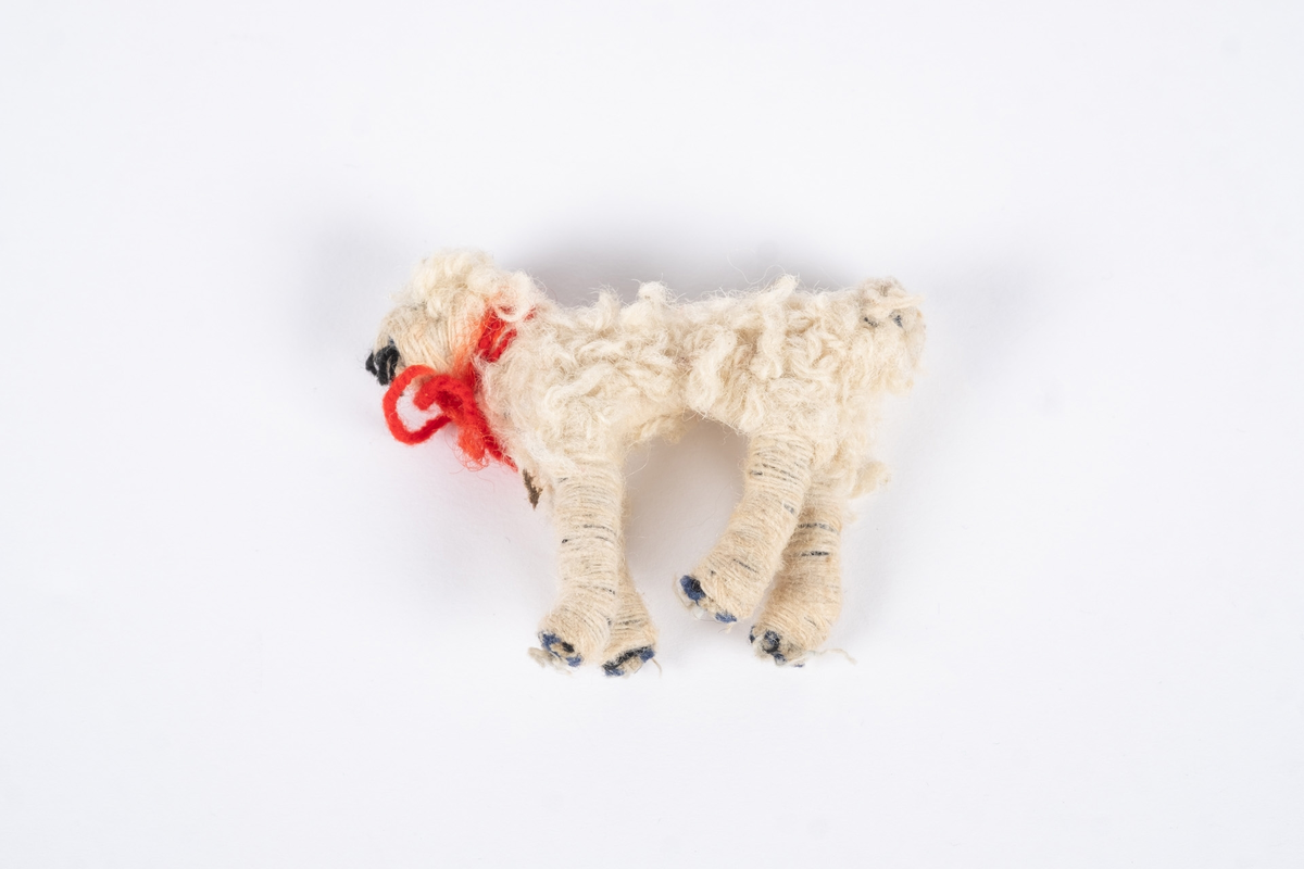 En hundefigur laget av tekstil og ull. Hunden er hvit med et rødt halsbånd.
