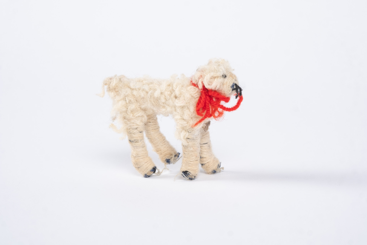 En hundefigur laget av tekstil og ull. Hunden er hvit med et rødt halsbånd.