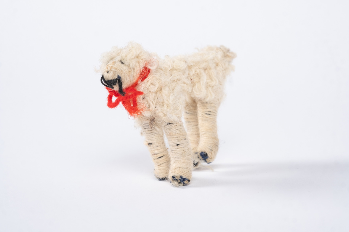 En hundefigur laget av tekstil og ull. Hunden er hvit med et rødt halsbånd.