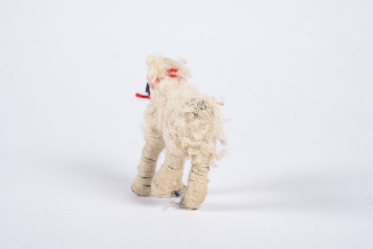 En hundefigur laget av tekstil og ull. Hunden er hvit med et rødt halsbånd.