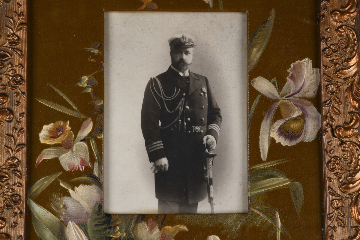 Tre enkeltportrett i samme ramme. En eldre mann med skjegg i marineuniform, øverst, kvinne i midten med enkeslør, ung mann med cravatte og slipsnål nederst. Passepartout er dekorert med håndmalte blomster, rammen er forgylt med dekor i nyrokkostil.