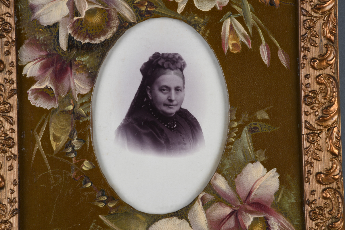 Tre enkeltportrett i samme ramme. En eldre mann med skjegg i marineuniform, øverst, kvinne i midten med enkeslør, ung mann med cravatte og slipsnål nederst. Passepartout er dekorert med håndmalte blomster, rammen er forgylt med dekor i nyrokkostil.