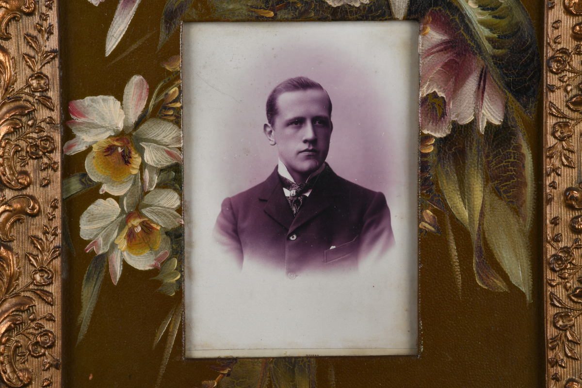 Tre enkeltportrett i samme ramme. En eldre mann med skjegg i marineuniform, øverst, kvinne i midten med enkeslør, ung mann med cravatte og slipsnål nederst. Passepartout er dekorert med håndmalte blomster, rammen er forgylt med dekor i nyrokkostil.