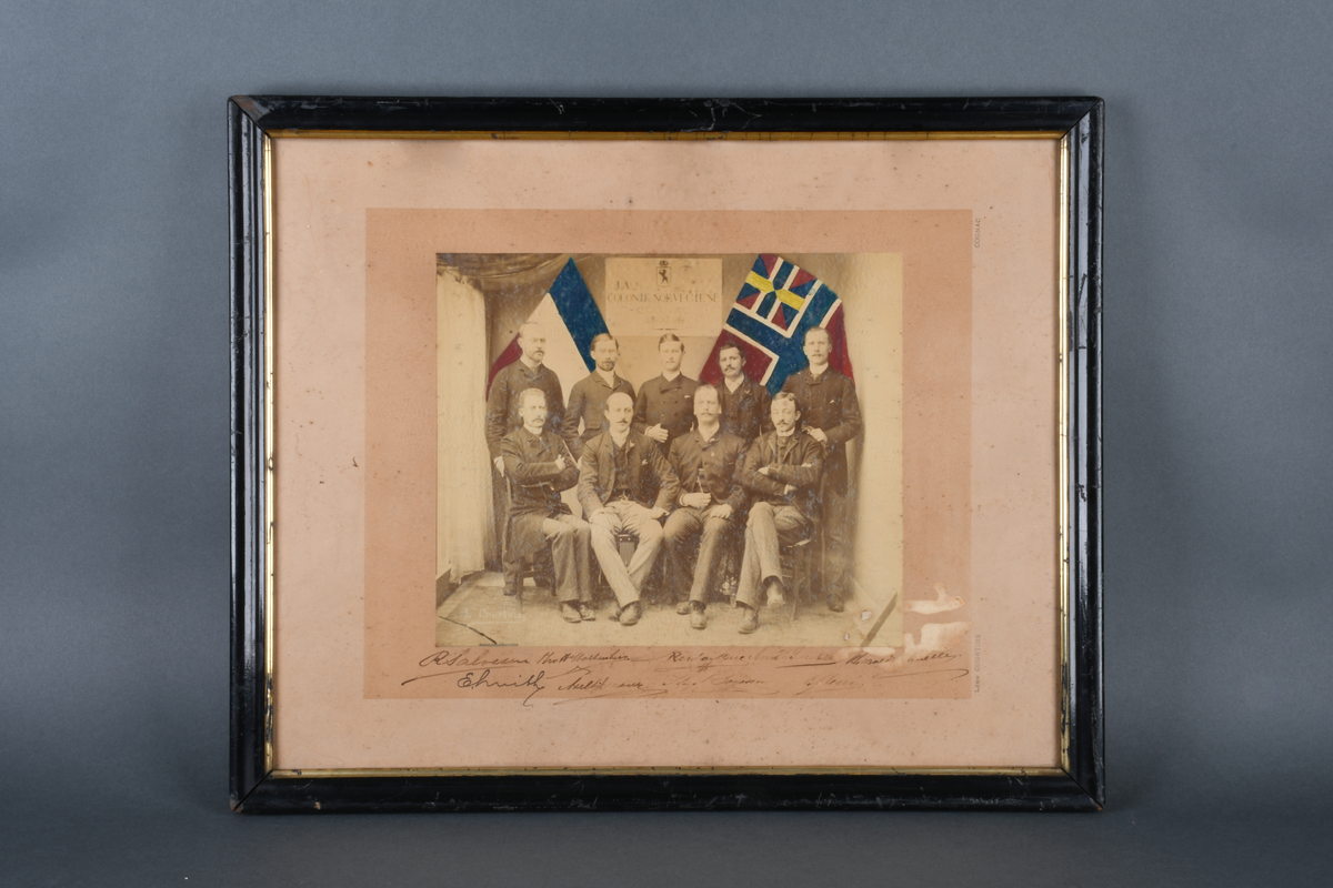 Gruppefotografi av ni menn, norskt handelsflagg og fransk nasjonalflagg i bakgrunnen. Ni signaturer under fotografiet.