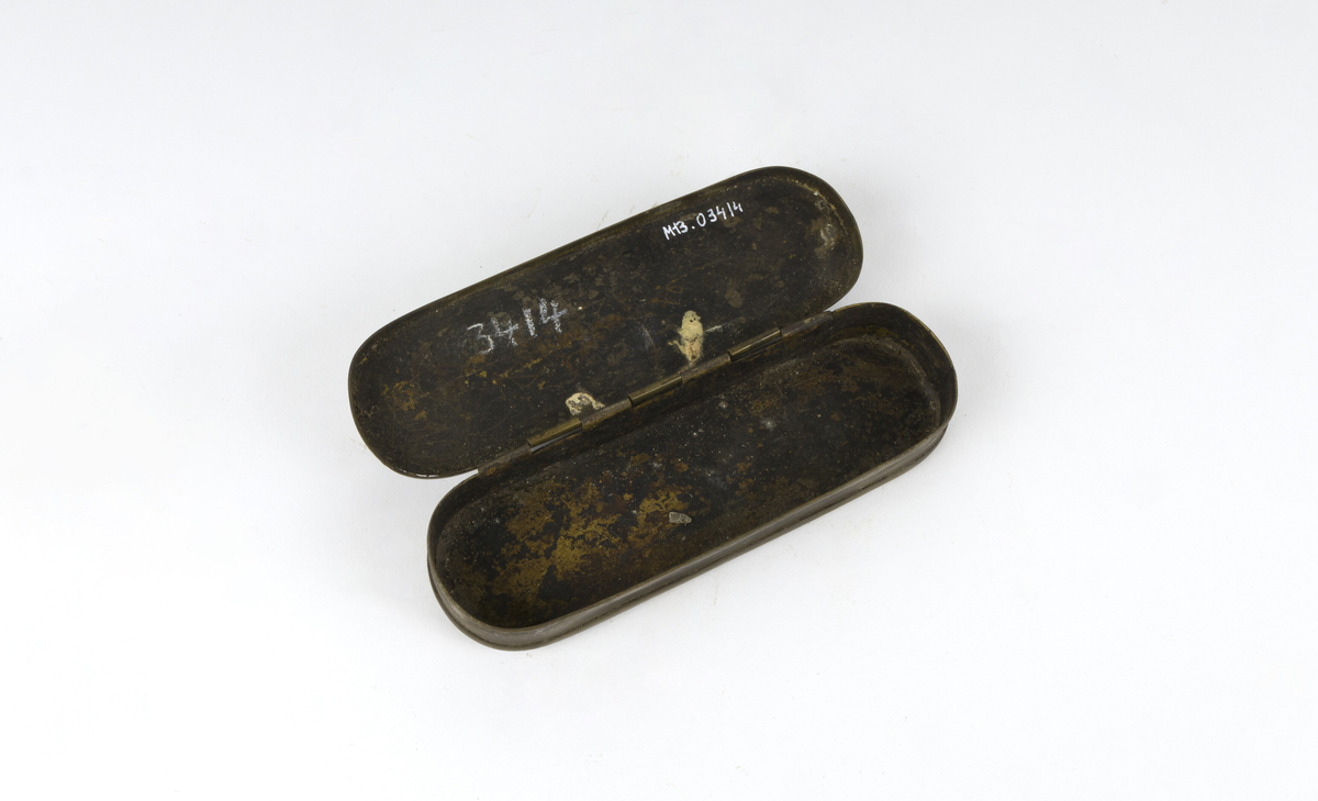 Dåse, tobakksdåse. Avlang oval snusdåse av messing med avrundede hjørner. Har en påsatt og påklinket utenpåliggende bunn og utenpåliggende, hengslet lokk.