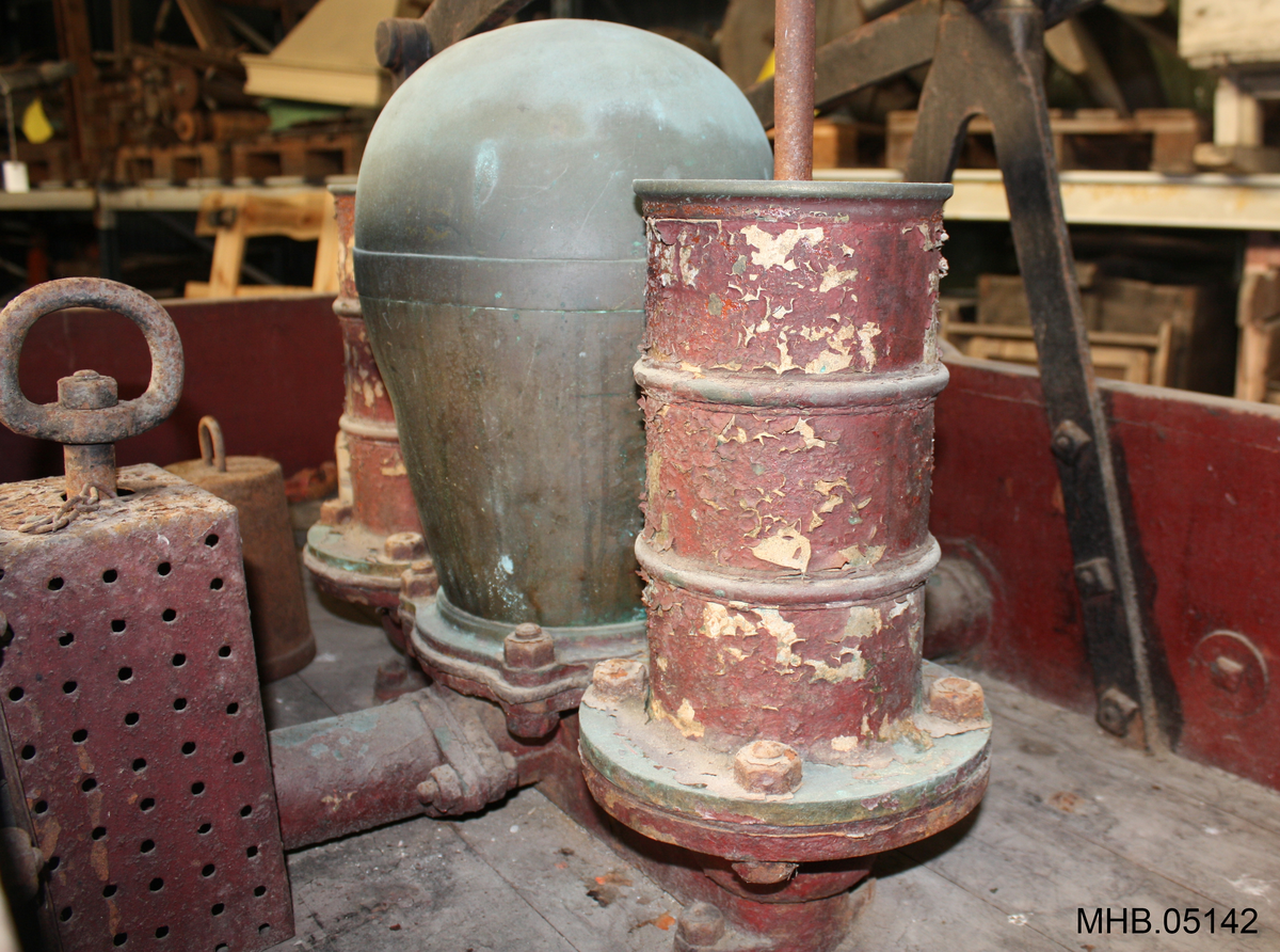4-hjult vogn med montert håndpumpe og tilførselsslange. To store og to små hjul. Oval plate med navn på produsent fremme og bak på vognkassen.