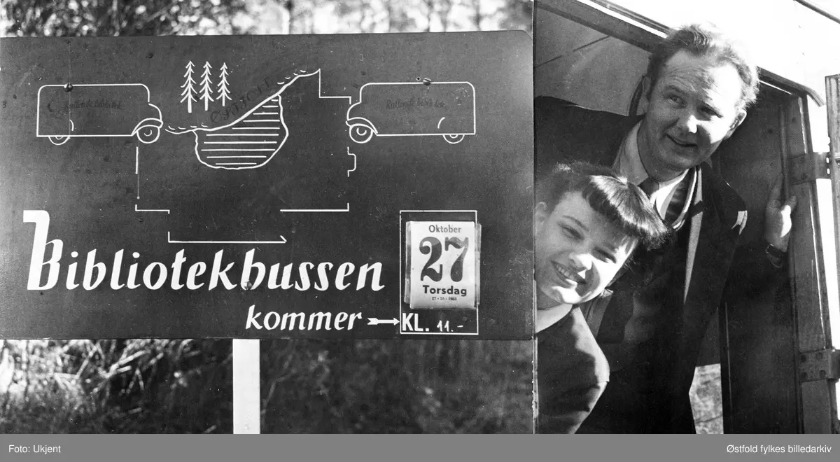 Bokbussen fra Østfold sentralbibliotek i Fredrikstad besøker Varteig i 1955. Sjåfør Viggo Nilsen og bibliotekar Kirsten-Betty  Johannessen fra Østfold sentralbibliotek i Fredrikstad ved datoskilt på en av de faste oppslagsplakatene for bokbussens ankomsttid  (som var laget etter amerikansk system).  
I 1955 hadde bokbussen i Østfold  50 000 årlige utlån av bøker. Folk møtte opp til faste holdeplasser på faste dager, hver fjerde uke. Det var også mulig å bestille bøker. Om sommeren var bokbussens ruter innstilt.
Viggo Nilsen startet som sjåfør for bokbussen ca. 1951-52, og kjørte hver eneste rute, mens bibliotekarene i Fredrikstad skiftet på å være med. Nilsen arbeidet som bokbussjåfør til han ble pensjonist i 1984.
Skilt: "Bokbussen kommer", se Avbildet obkekt.