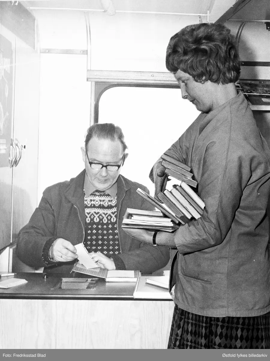 Bibliotekbussen er på Vallefjellet, Rolvsøy i januar 1973. Bokbussjåfør og bibliotekfullmektig Viggo Nilsen ekspederer ukjent låner som leverer inn bøker.