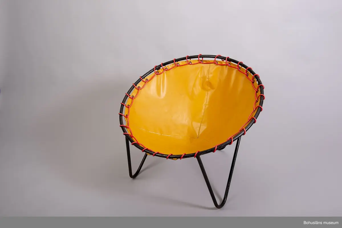 Fåtölj med stomme av svartmålade stålrör med sits av PVC-bestruken bomullsväv. Sitsen i form av en påse eller säck, fästad runt ramen med plastat snöre,  snörat i metallklädda hål.
Okänd tillverkare.
