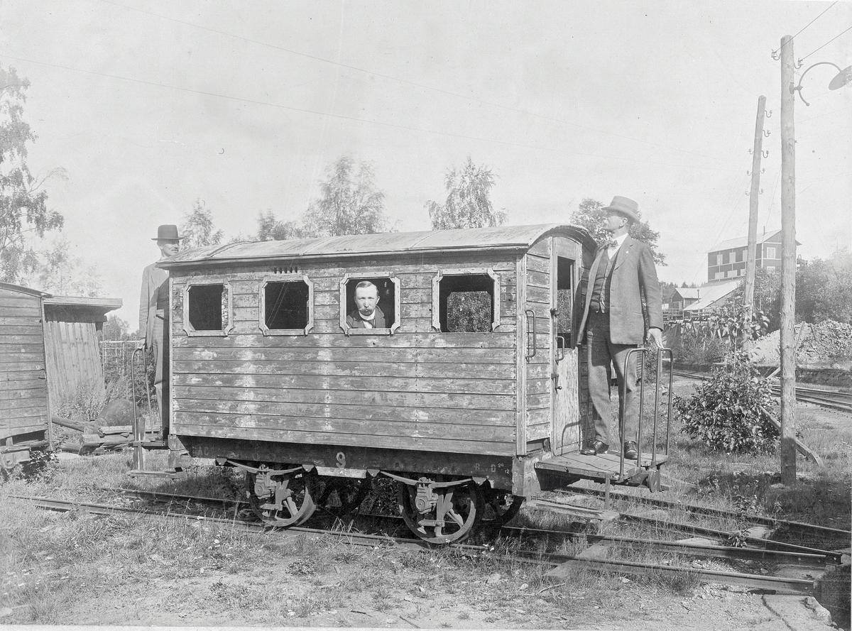 Vikern-Möckeln järnväg. Tågvagn av trä på räls med tre personer i och vid. Handskriven text under "Dalkarlsbergs järnväg I och III kl. vagn. Personer: Te Hildebrand, Miö Lundqvist, Ti Steele ".